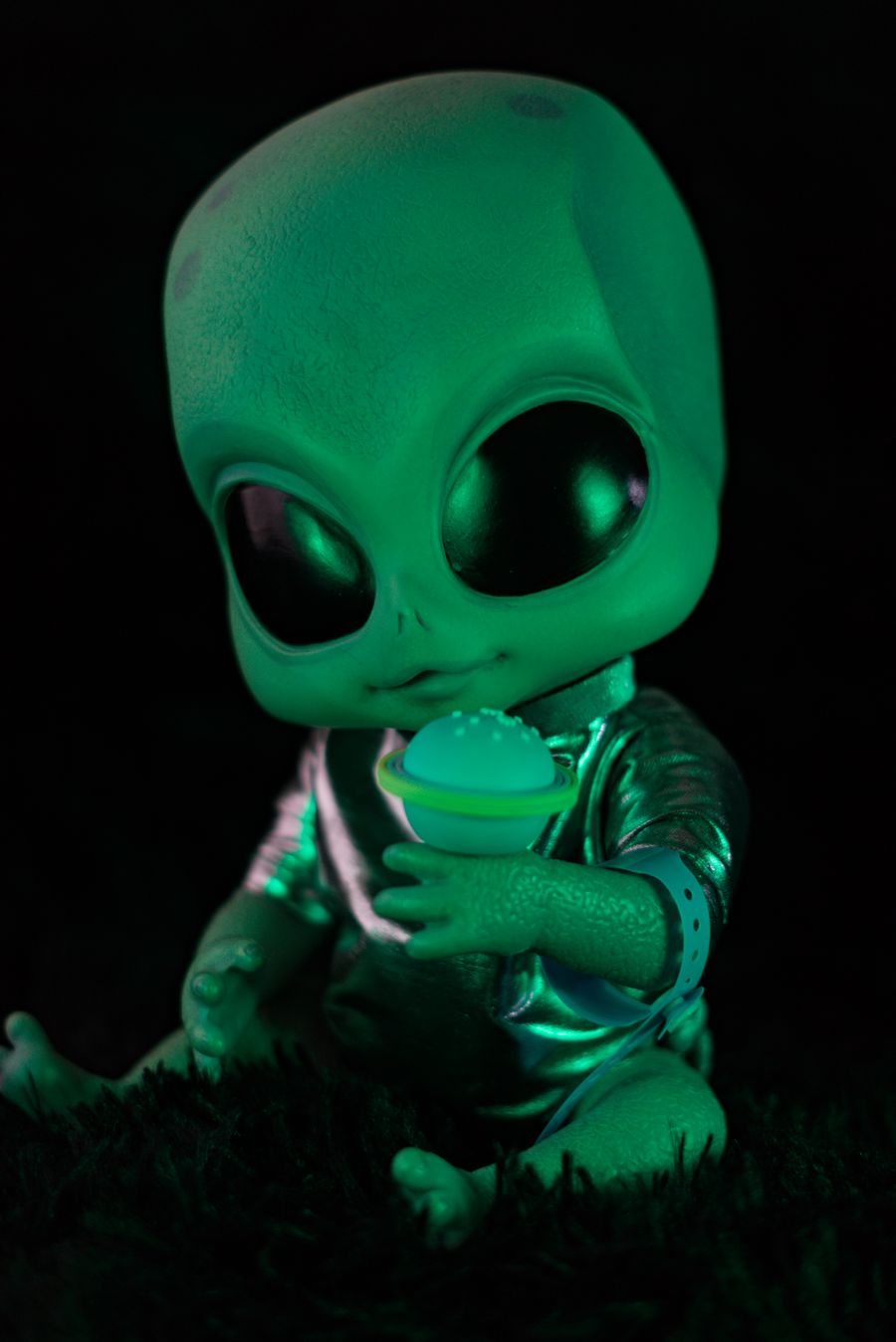 Bebê alienígena verde e fofo, de olhos grandes, segurando um pequeno planeta